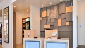 A reception area with a counter, a wall-mounted information board, and a shelf with snacks. - Holiday Inn Express & Suites Southgate - Detroit Area by IHG (Southgate)