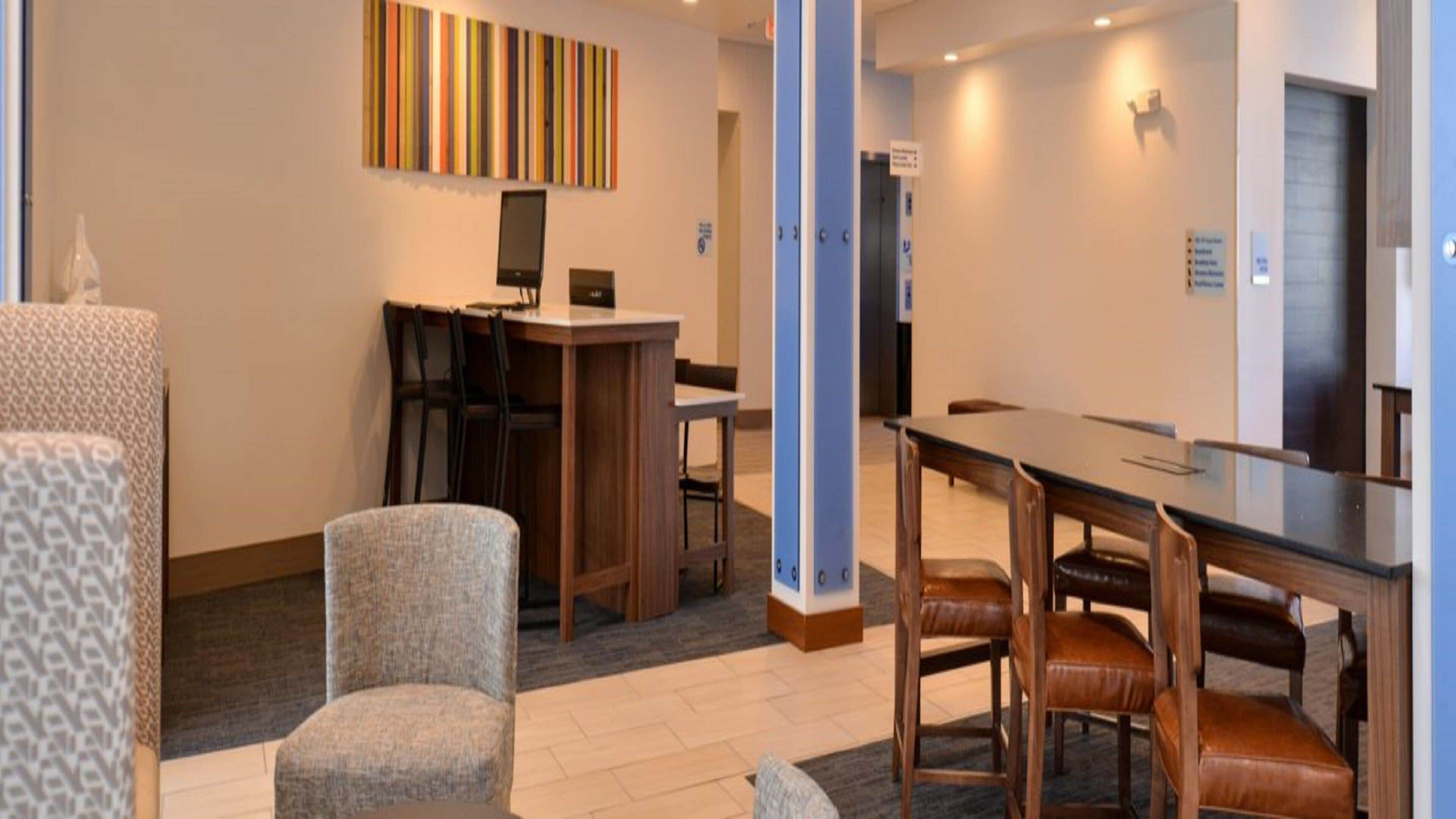 A hotel room with a dining area, a desk with a computer, and a seating arrangement with chairs and a table.