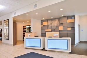 A hotel reception area with two reception desks, a market, and a wall with informational posters. - Holiday Inn Express & Suites Southgate - Detroit Area by IHG (Southgate)