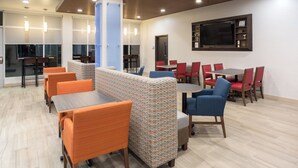 A modern lounge area with seating arrangements, a flat-screen TV mounted on the wall, and a wooden ceiling.