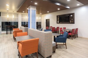 A modern lounge area with seating arrangements, a flat-screen TV mounted on the wall, and a wooden ceiling.