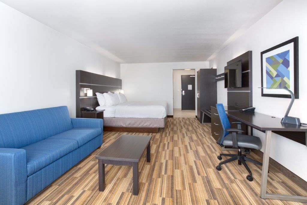 A hotel room with a bed, a blue sofa, a desk with a chair, a TV, and a wooden floor.