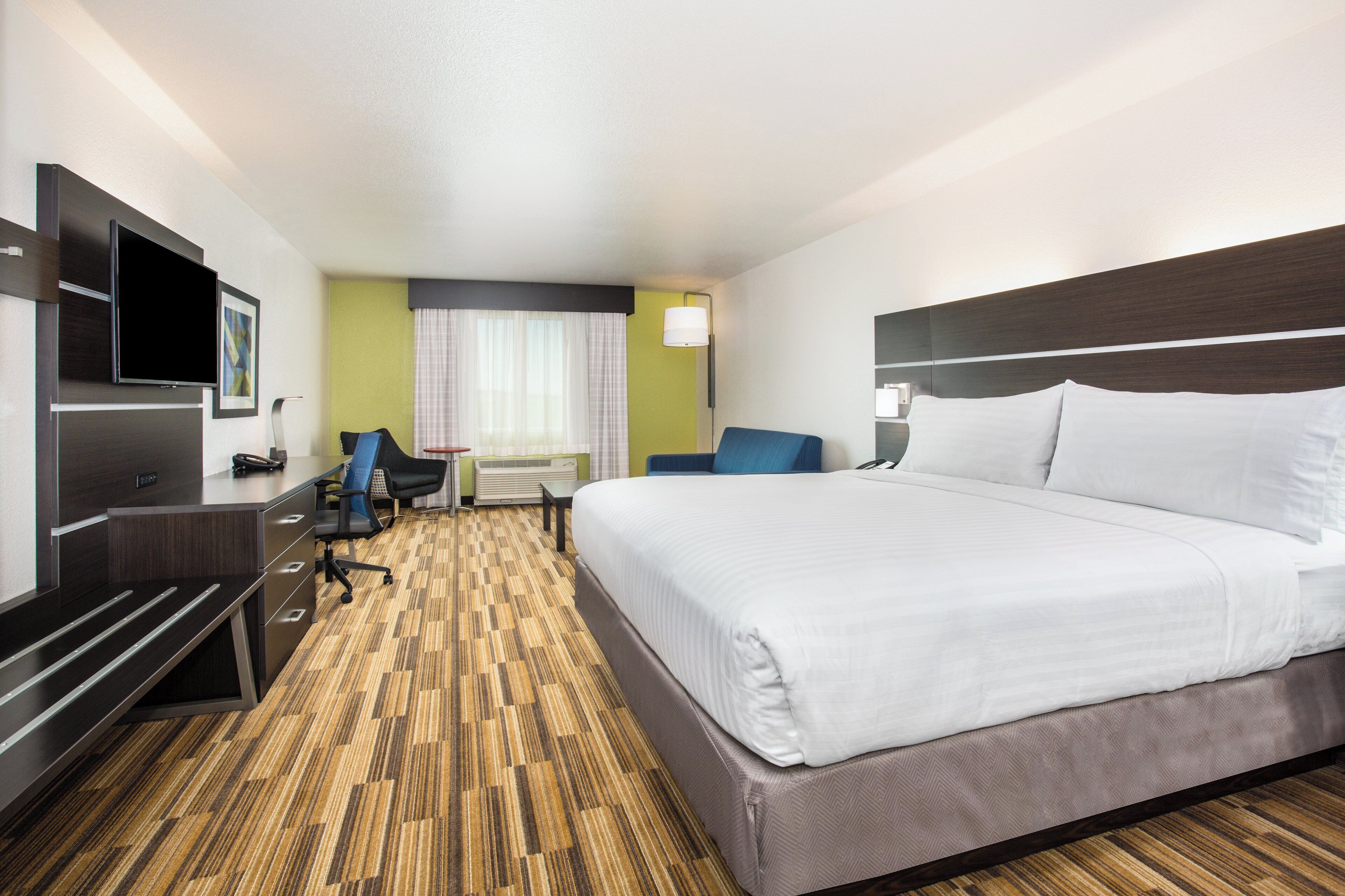 Une chambre d’hôtel avec un grand lit, un bureau, une chaise, une télévision et une fenêtre avec des rideaux.