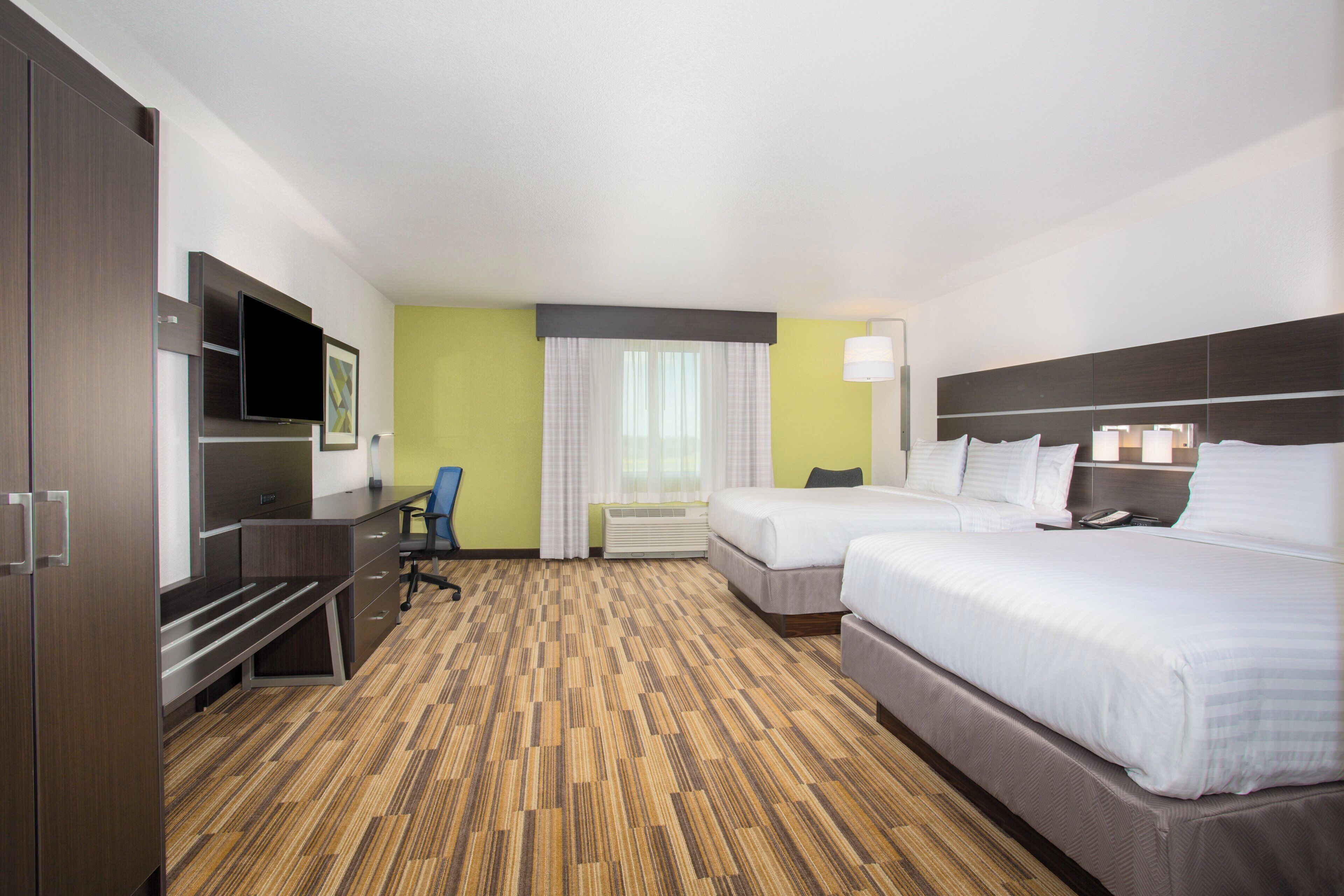 A hotel room with a bed, a desk, a chair, a television, and a window with curtains.
