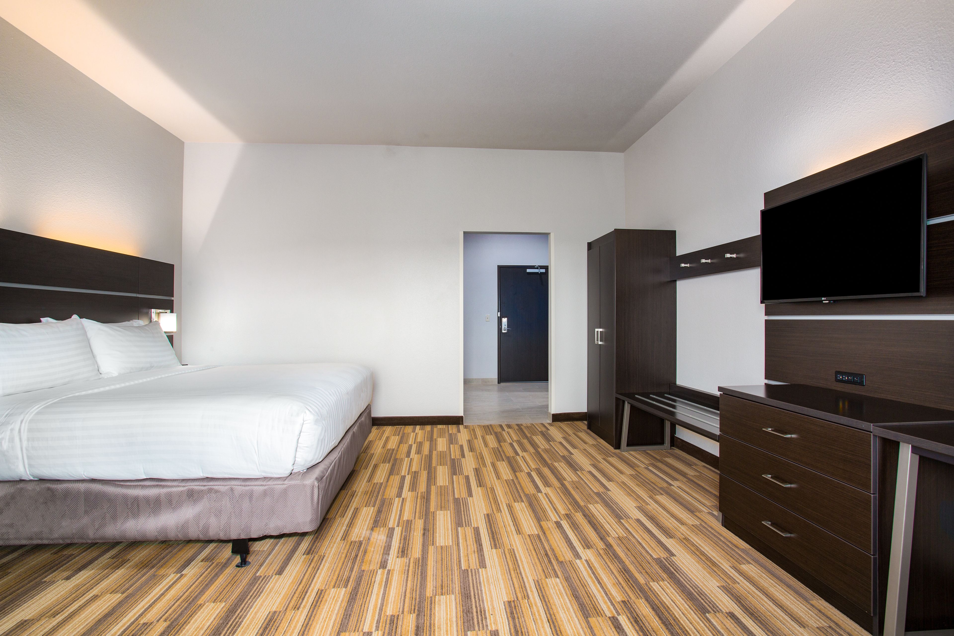 Una habitación de hotel con cama, televisor, armario y suelo de madera.