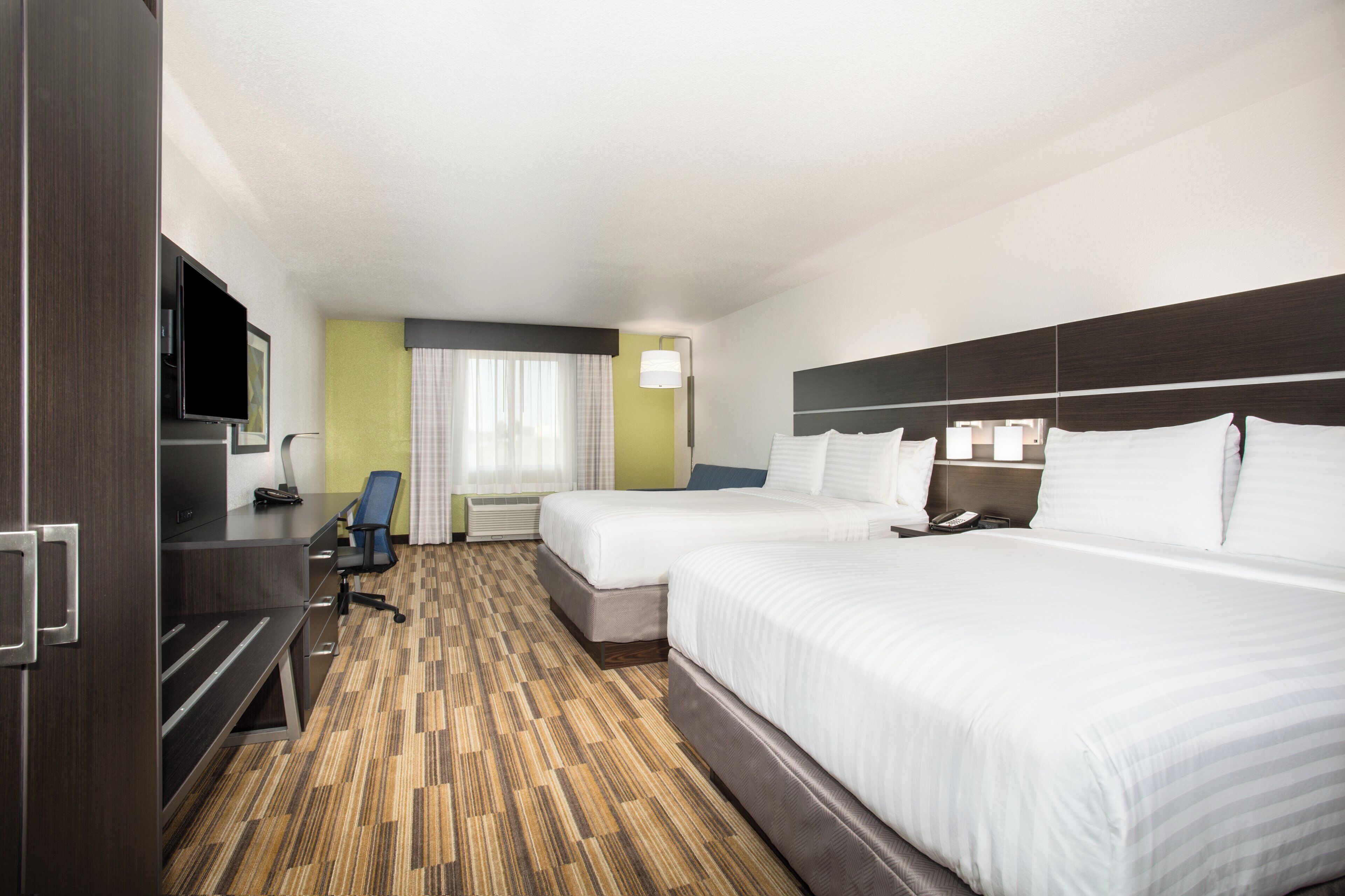 Habitació d'hotel amb dos llits, una taula, una cadira, un televisor i una finestra amb cortines.