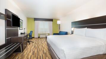 Ett hotellrum med en stor säng, ett skrivbord med en stol, en tv och ett fönster med gardiner.