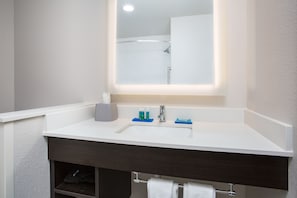 Un baño con lavamanos blanco, tocador oscuro y espejo sobre el lavamanos.