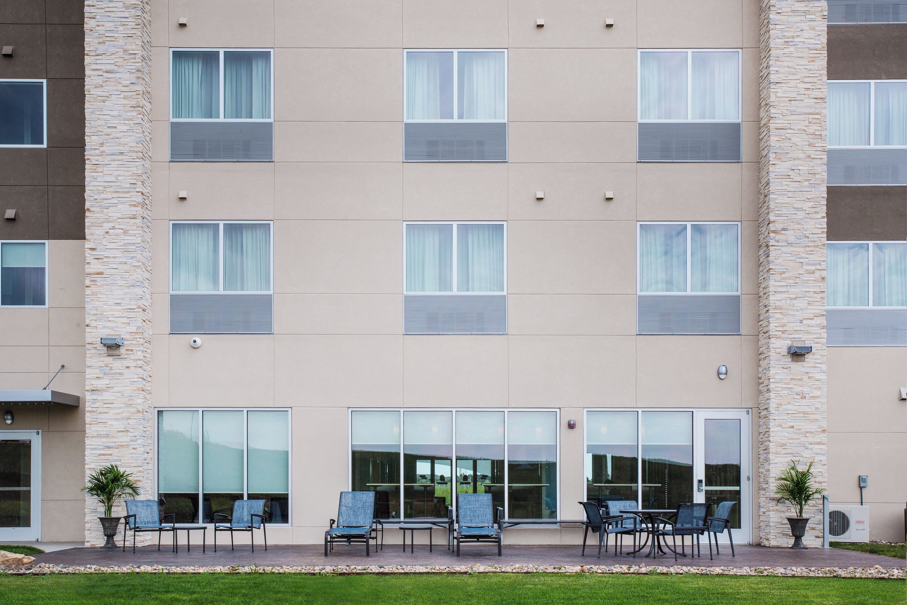 Un immeuble à plusieurs étages doté d’une façade sobre, de grandes fenêtres et d’un espace extérieur aménagé avec des chaises et des tables.