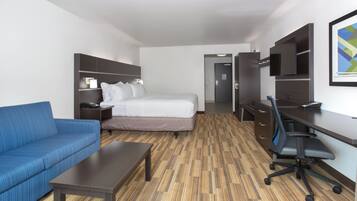 Una habitación de hotel con una cama, un sofá azul, un escritorio, una silla y un televisor.