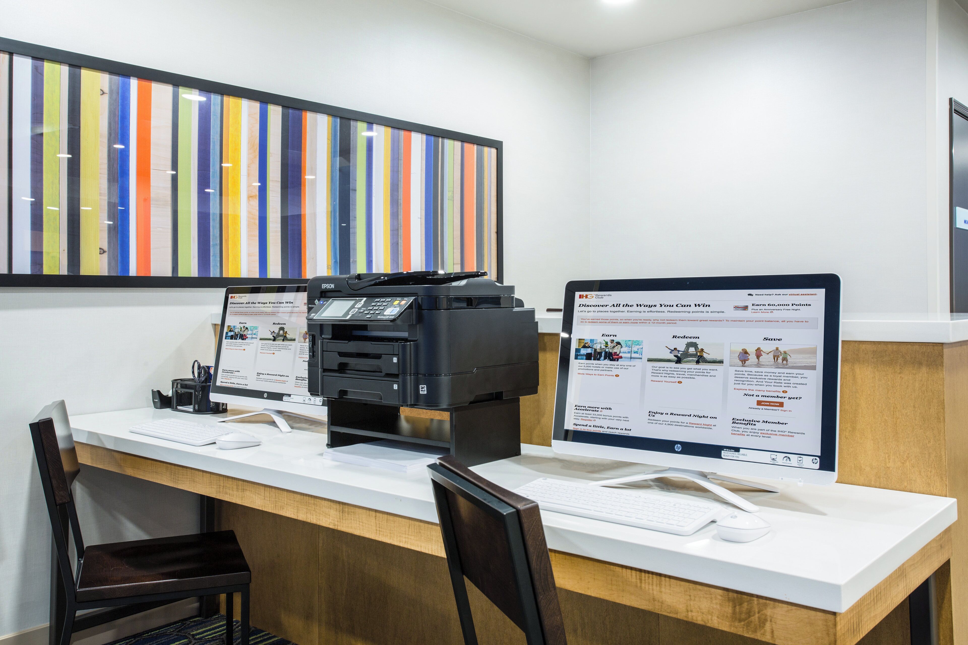 A reception desk with two monitors displaying a rewards program interface, a printer, and a keyboard.
