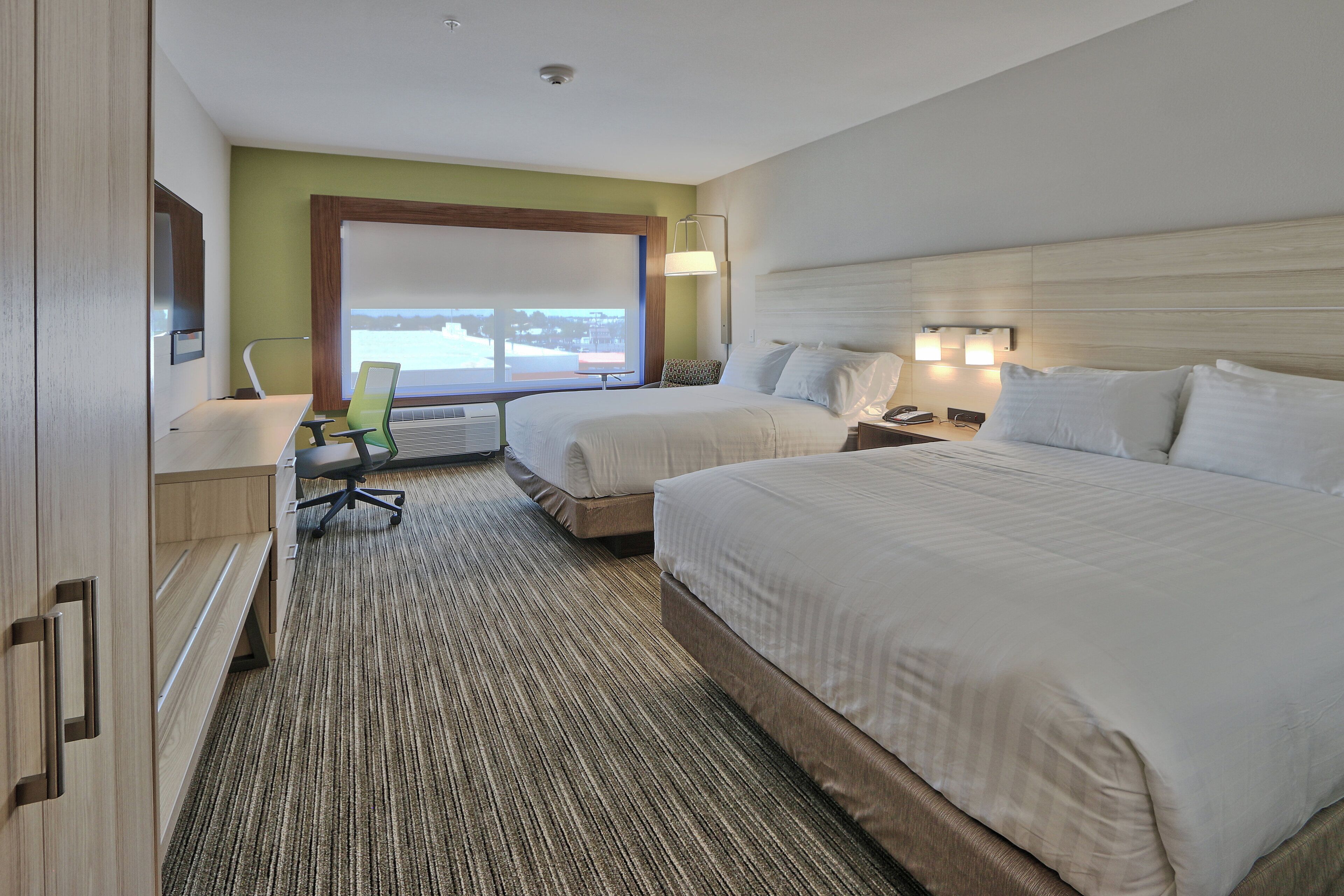 A hotel room with two beds, a desk, a chair, and a large window.