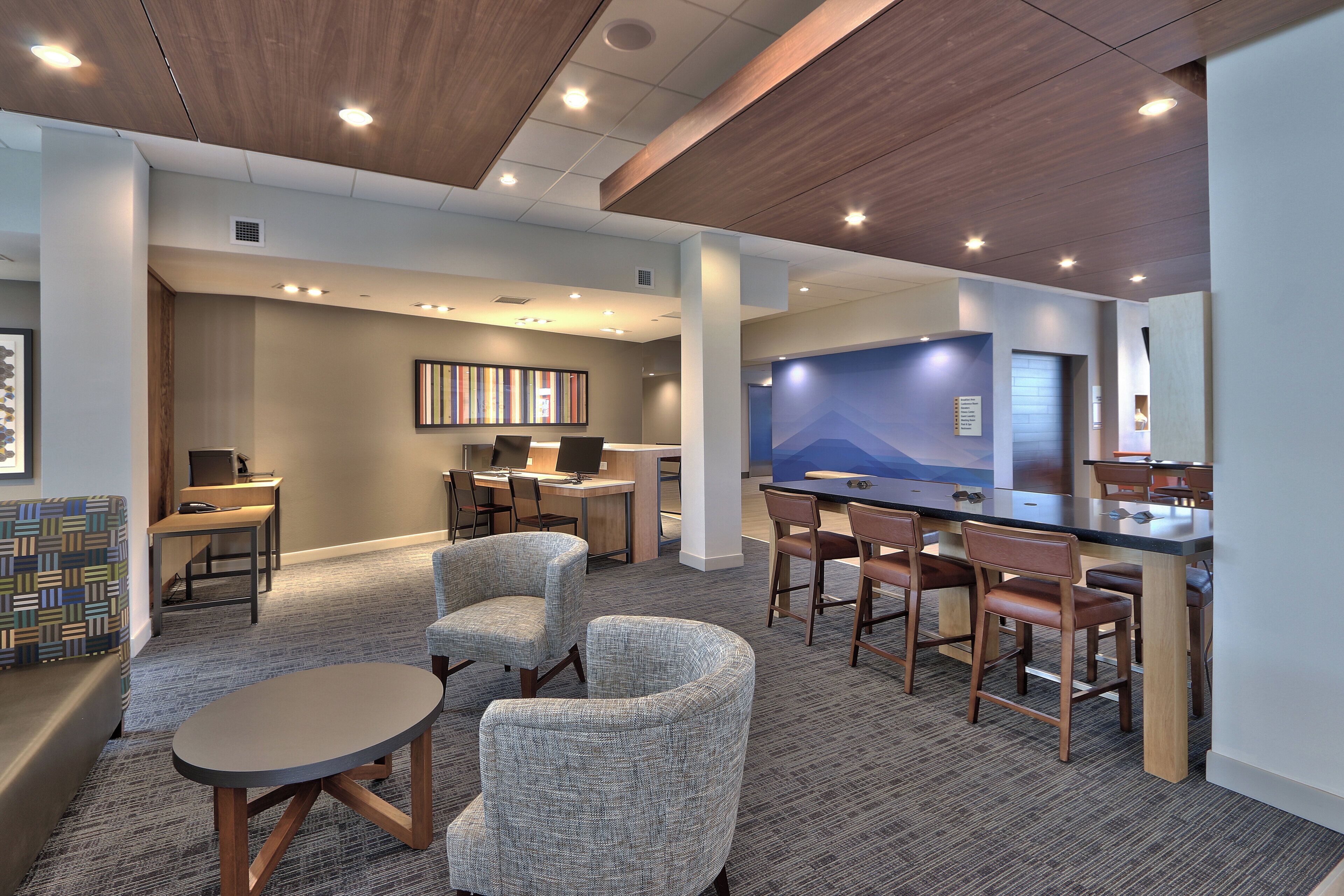A modern hotel lobby with a bar area, seating, and a large screen.