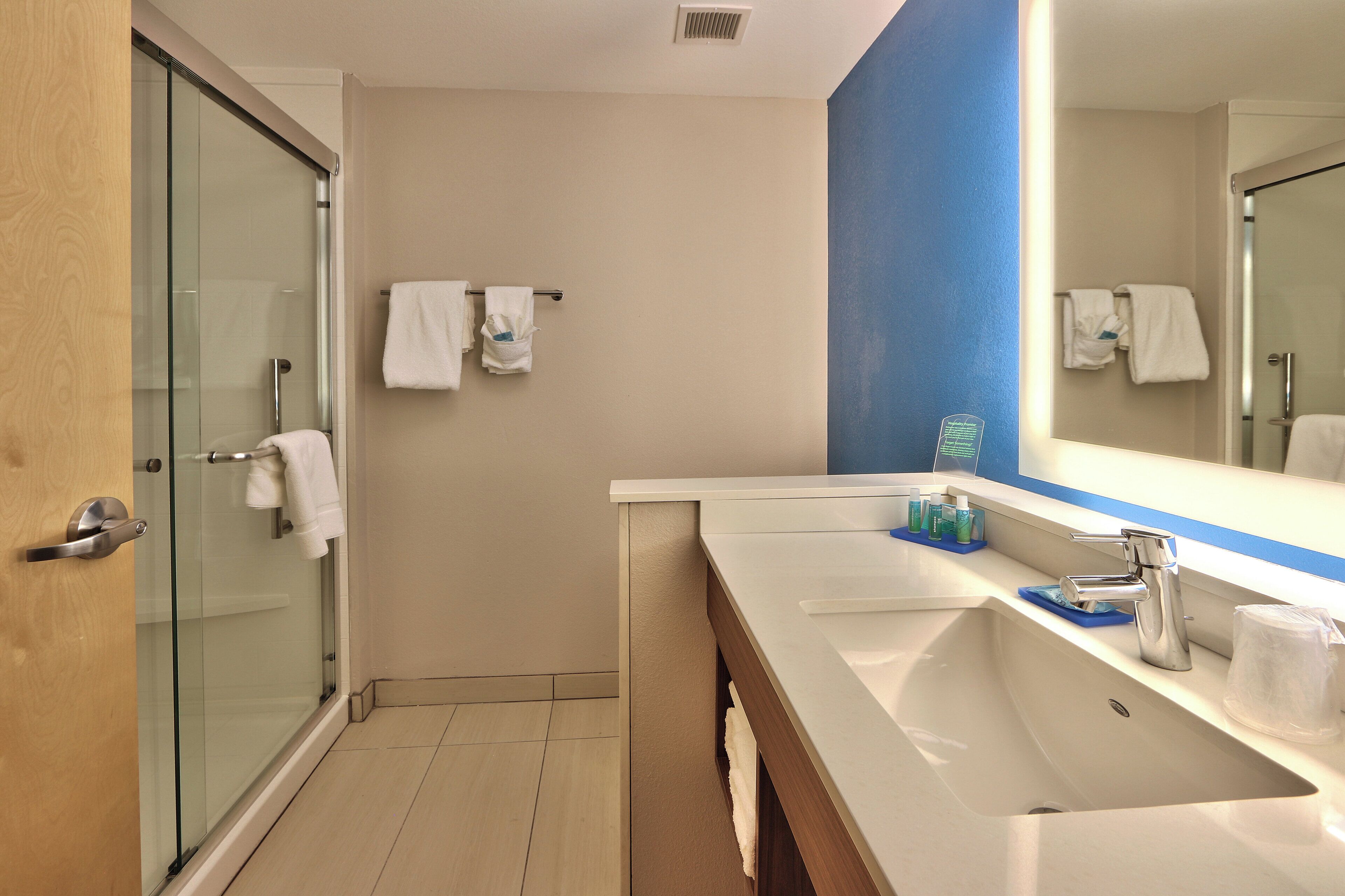 A modern bathroom with a glass shower enclosure, a large mirror, and a vanity with a sink and toiletries.