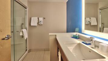 A modern bathroom with a glass shower enclosure, a large mirror, and a vanity with a sink and toiletries.