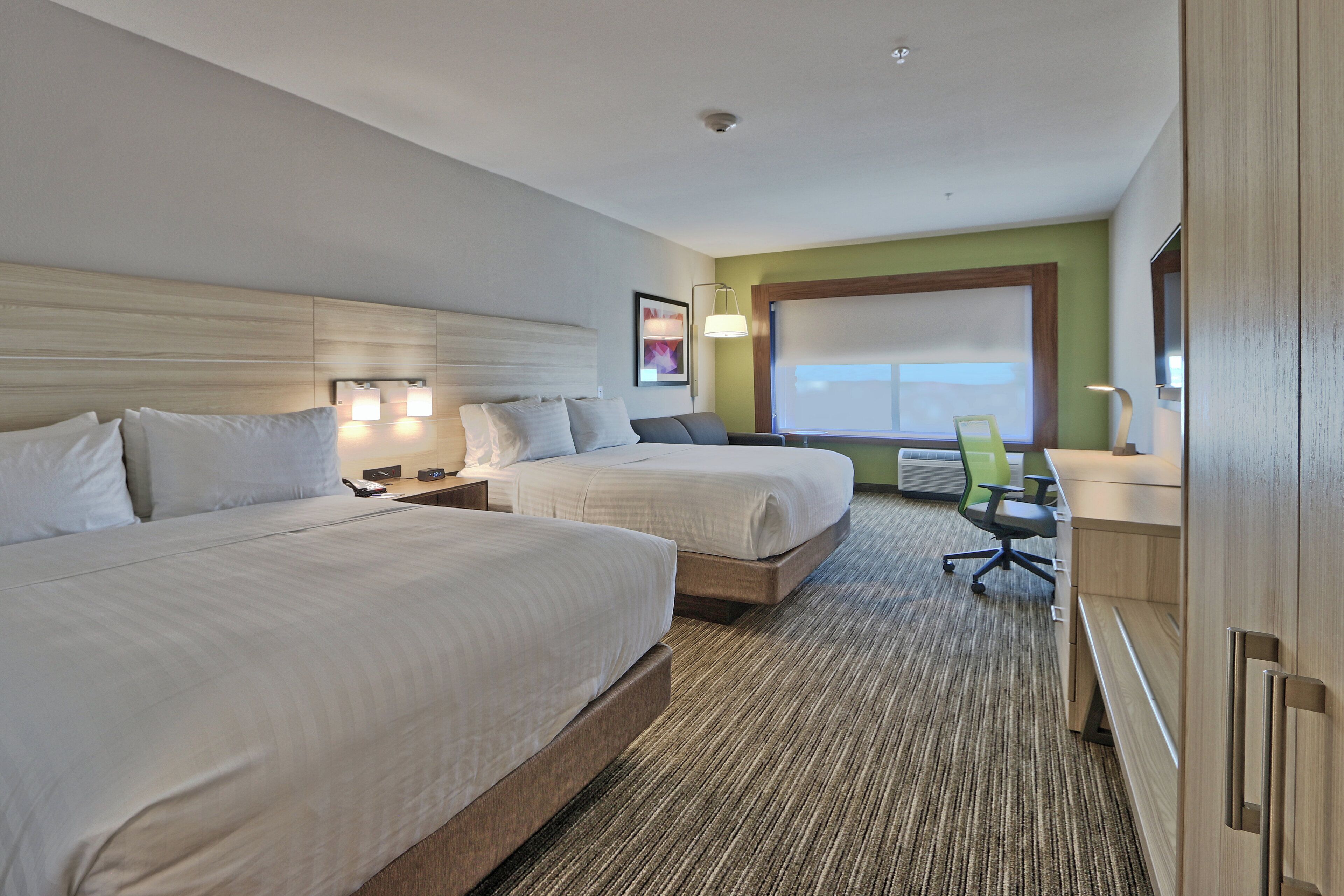 A hotel room with two beds, a desk, a chair, and a large window.
