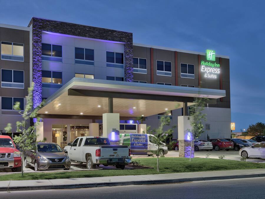 A Holiday Inn Express & Suites hotel with a covered entrance, multiple parking spaces, and a clear sky.