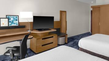 A hotel room with a desk, a television, a chair, two beds, and a wardrobe.