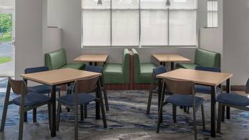A dining area with green cushioned booths and wooden tables, carpeted floor, and large windows with blinds.