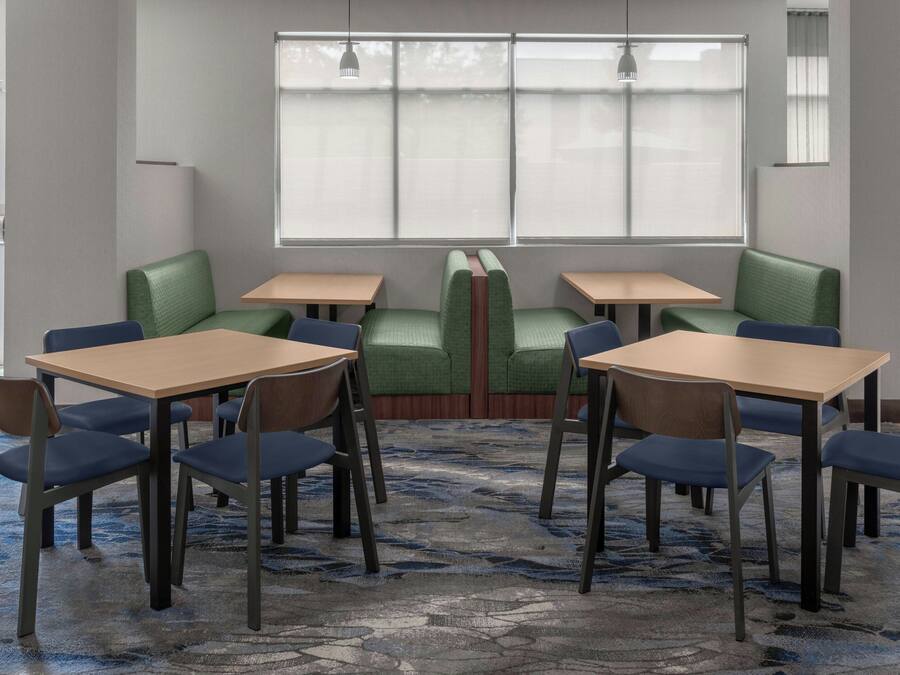 A dining area with green cushioned booths and wooden tables, carpeted floor, and large windows with blinds.