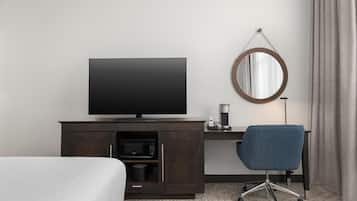 Une chambre d’hôtel avec un lit, un bureau doté d’une télévision, une machine à café et un miroir rond accroché au mur.