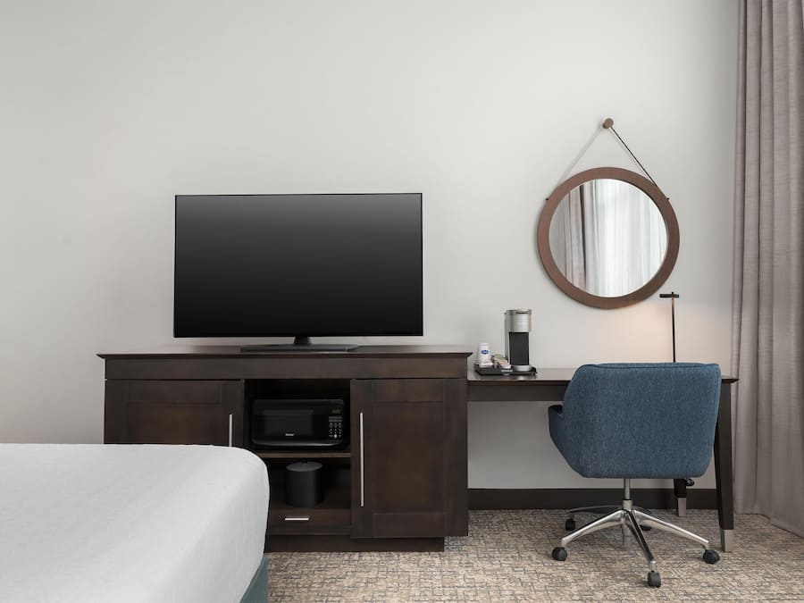 Ein Hotelzimmer mit einem Bett, einem Schreibtisch mit Fernseher, einer Kaffeemaschine und einem runden Spiegel an der Wand.