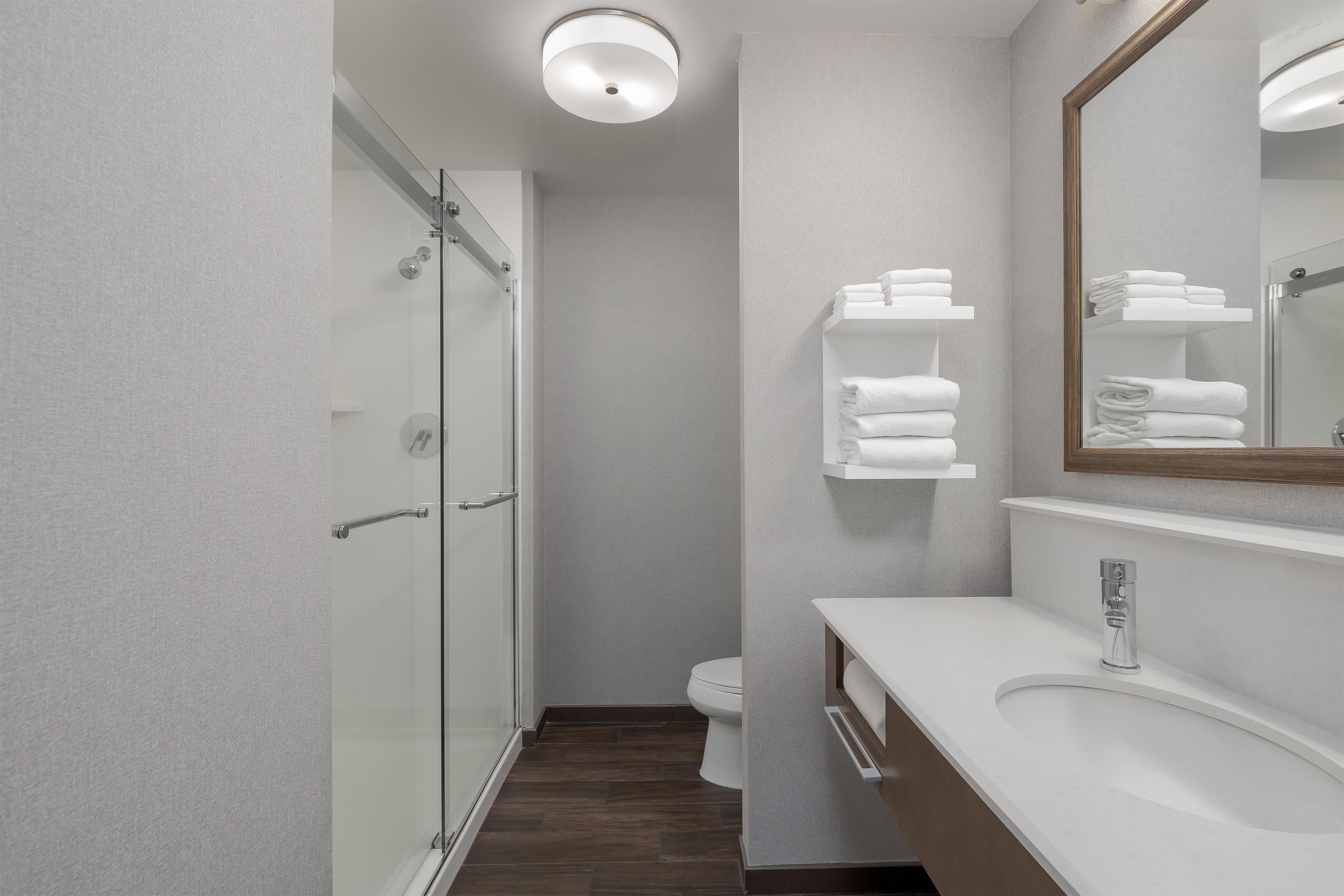 A modern bathroom with a glass shower enclosure, a white sink, and a mirror with a wooden frame.