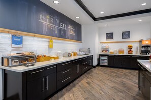 Een moderne keuken met een prikbord waarop culinaire zinnen staan, een koffieapparaat en diverse etenswaren op het aanrecht.
