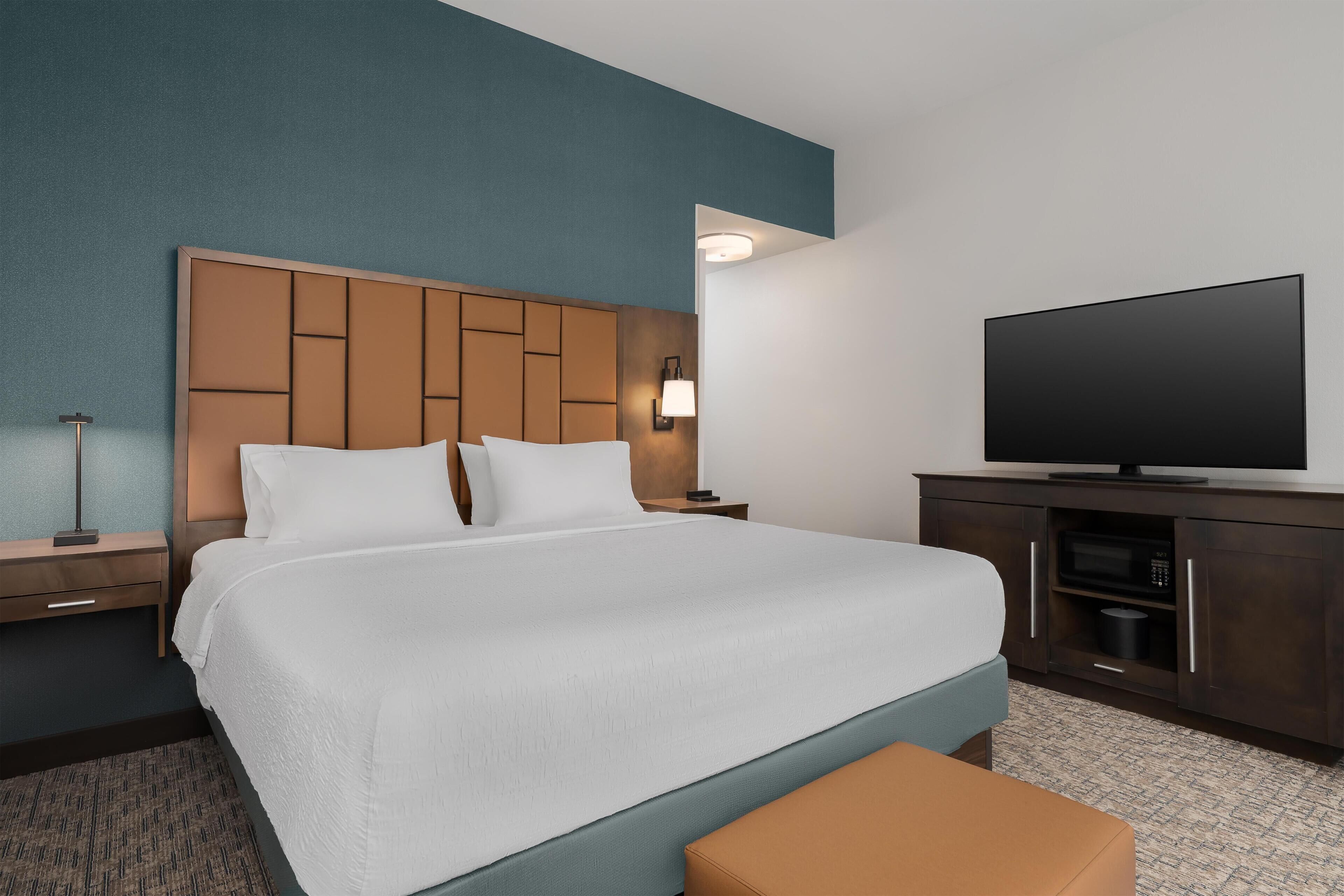 A hotel room with a bed, a television, a nightstand, and a desk.