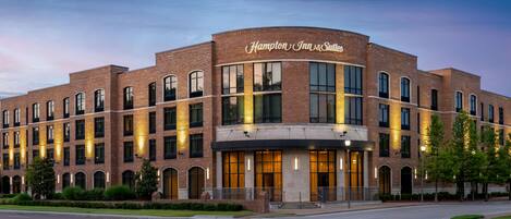 Un hotel Hampton Inn & Suites con fachada de ladrillo, ventanas grandes y una entrada bien iluminada.