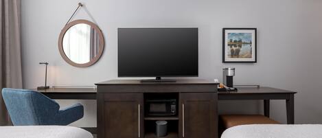 Hotelkamer met een flatscreen televisie, een ingelijst schilderij, een ronde spiegel en een minibar.