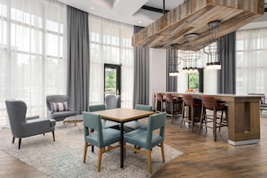 A modern hotel room with a dining area, large windows with sheer curtains, and a bar with stools. - Hampton Inn & Suites Memphis Germantown (Germantown)