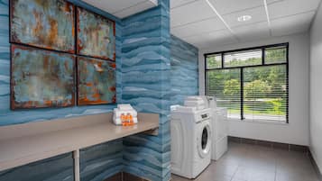 Une buanderie équipée d’un lave-linge, d’un étendoir et d’une étagère où sont rangées des serviettes et des bouteilles de lessive.