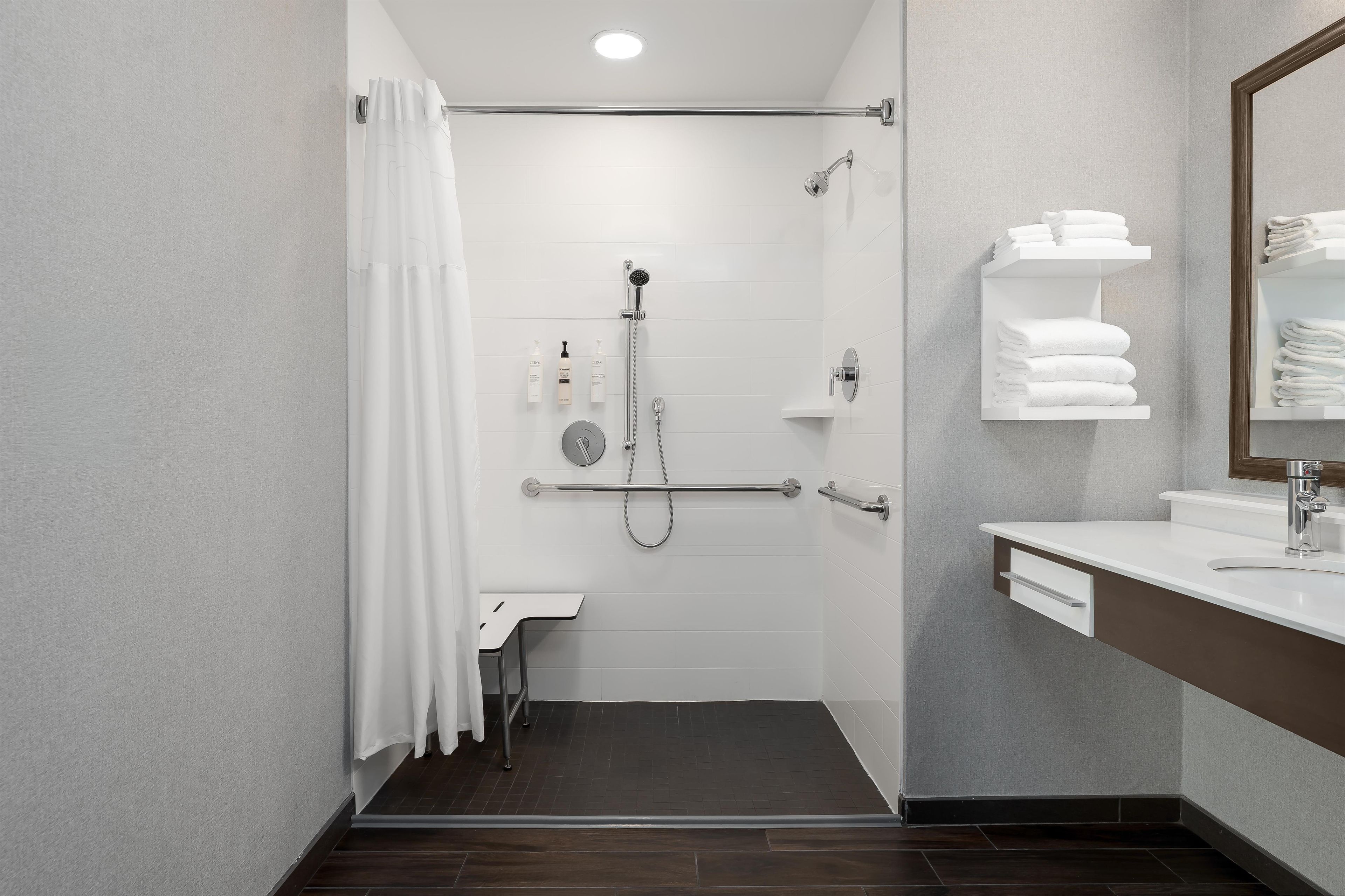 A modern bathroom with a shower, a toilet, and a sink. There are towels and toiletries on the wall.