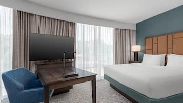 Une chambre d’hôtel comprenant un lit, un bureau avec un téléviseur à écran plat, une chaise, une lampe et une vue sur l’extérieur grâce à de grandes fenêtres.