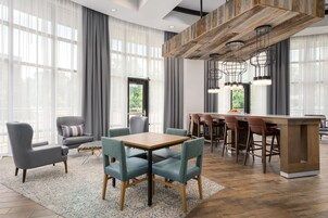 Habitación de hotel moderna con zona de comedor, ventanas amplias con cortinas translúcidas y barra con taburetes.