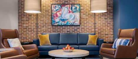 A modern lounge area with leather sofas, a round coffee table, and a large abstract painting on a brick wall.