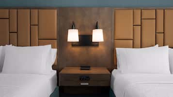 Et hotelværelse med to senge, et natbord med en lampe og et kontrolpanel.