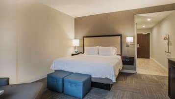 A hotel room with a large bed, bedside tables, a desk, and a chair. There is a door leading to another room.
