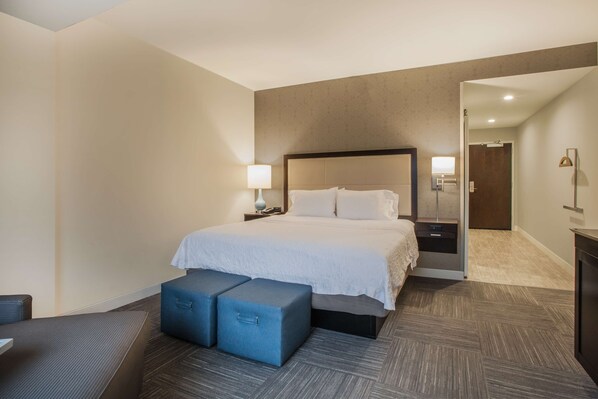 A hotel room with a large bed, bedside tables, a desk, and a chair. There is a door leading to another room.