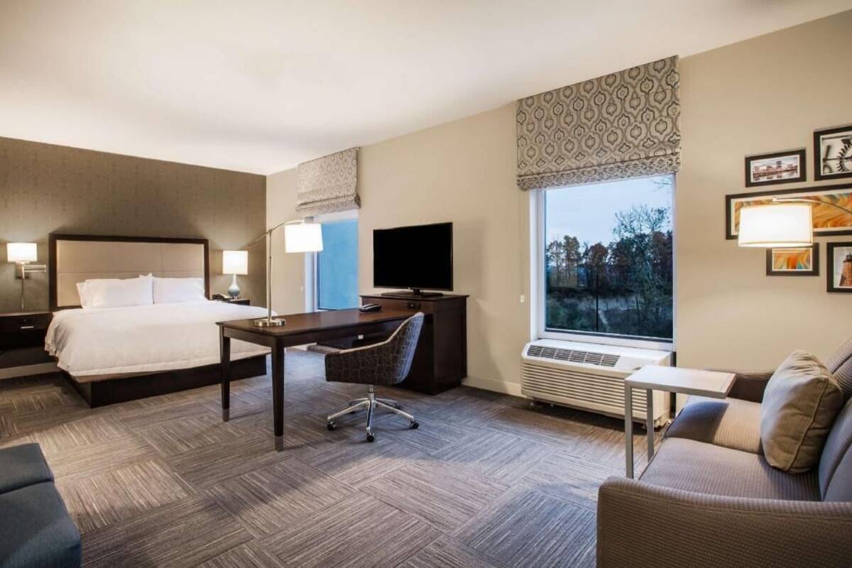 A hotel room with a bed, desk, chair, TV, and a sofa.