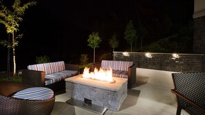 An outdoor patio with a stone fire table, wicker furniture, and a stone wall. - Hampton Inn Rochester Penfield (Rochester)