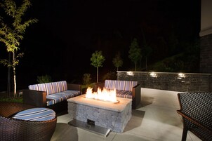 Un patio al aire libre con una mesa de fuego de piedra, mobiliario de mimbre y una pared de piedra.