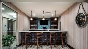 A bar area with a counter, stools, hanging lights, and a clock on the wall. - Hampton Inn Rochester Penfield (Rochester)