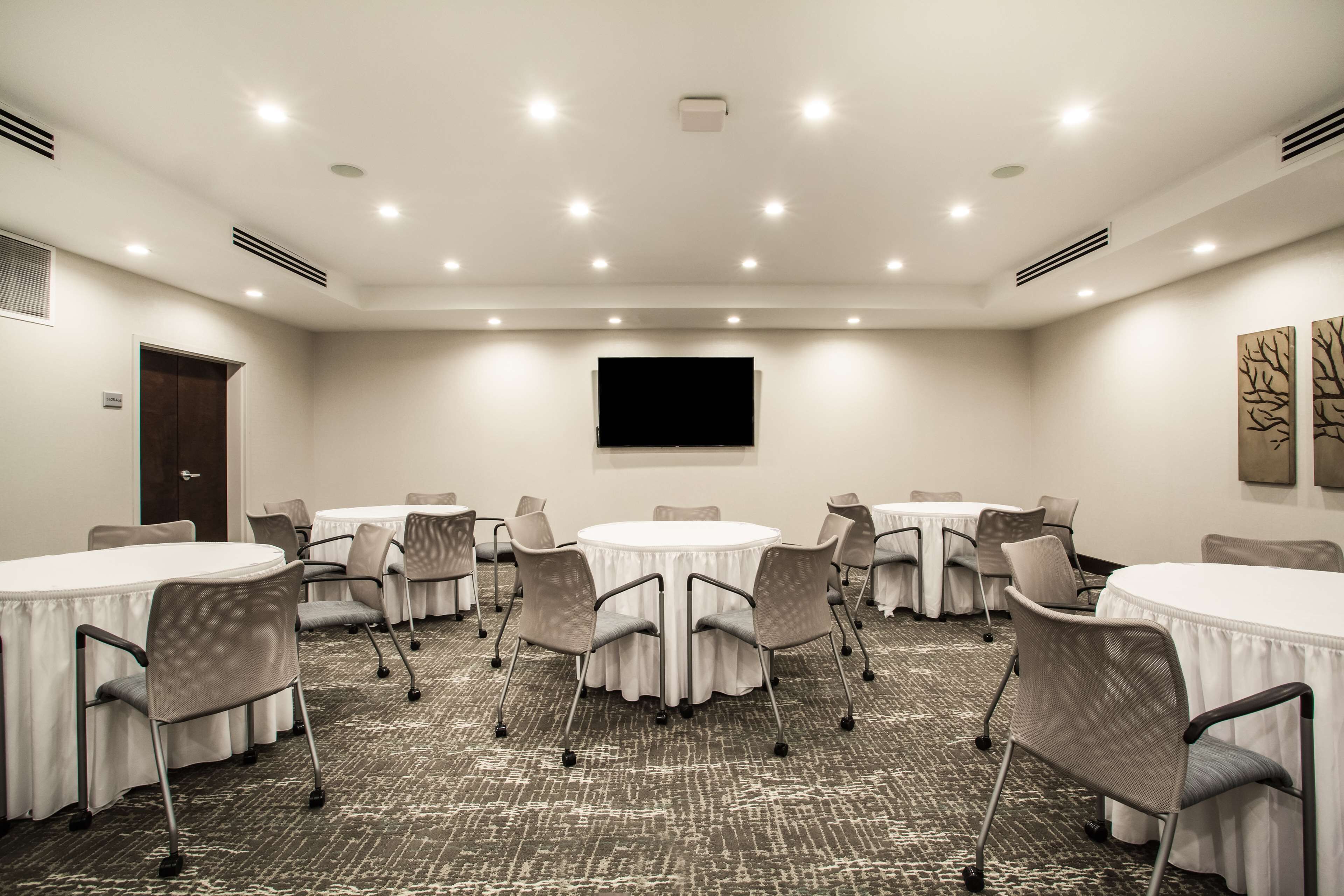 A conference room with round tables and chairs, a flat-screen TV, and a door.
