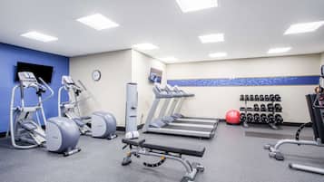 A gym with treadmills, elliptical machines, a bench press, and dumbbells.