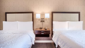 A hotel room with two beds, a nightstand with a lamp, and a small table with a phone and a remote control.