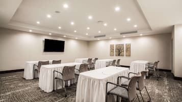 Une salle de conférence équipée de plusieurs tables et chaises, d’un téléviseur à écran plat fixé au mur et agrémentée d’œuvres d’art décoratives.