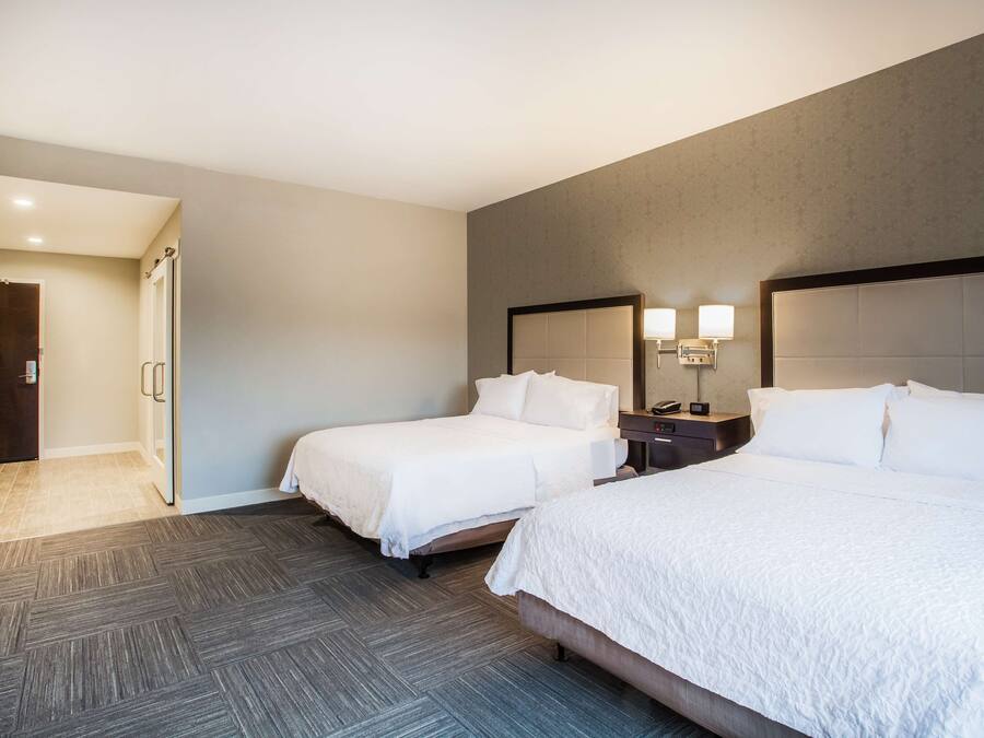 Habitación de hotel con dos camas, un baño y una mesita de noche con lámpara.