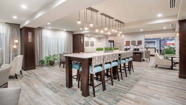 A spacious hotel lobby with a long reception desk, multiple seating areas, and a modern chandelier. - Hampton Inn Rochester Penfield (Rochester)